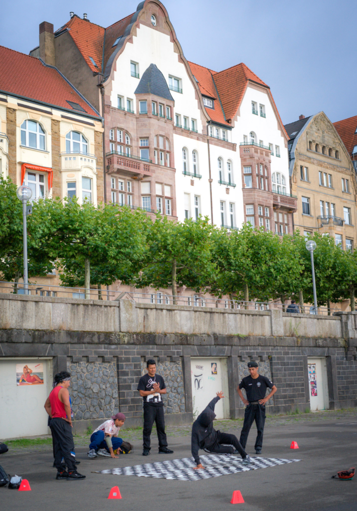 Performers dance on the concrete while onlookers take in the performance with a row of mill houses behind them