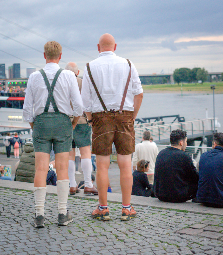 two men in white shirts and leiderhosen stand on the banks of the Rhineriver