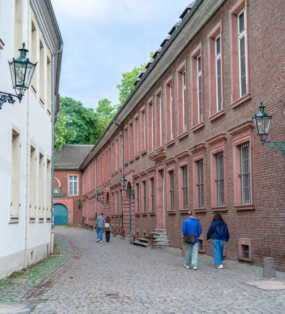 two people walk by a building that is red brick down an alleyway in Dusseldorf