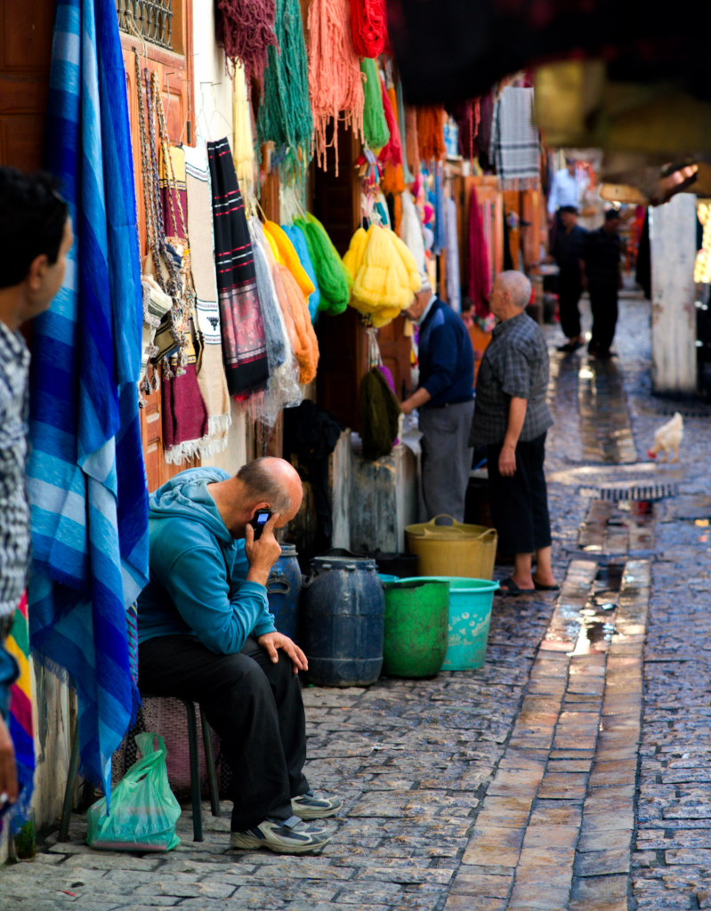 a man sits hunched over on a busy medina street in the fabric district of the Medina in Fes