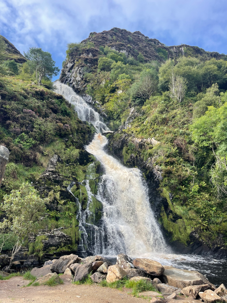 An outdoor scene with lush greenry and a waterfall coming down the side of it