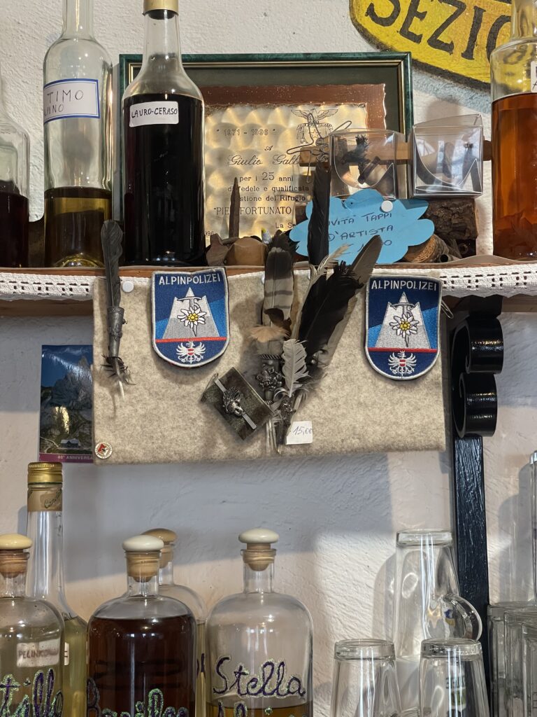 various patches from alpine associations and feathers hanging from a bar with old photos and grappa at Rifugio Calvi