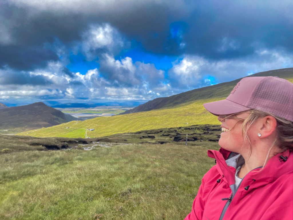 Woman with a pink hat and red rain jacket looks off in the distance on the Donegal Way in Donegal Ireland.