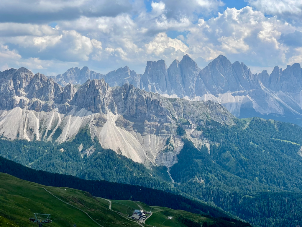 Dramatic view of jagged Dolomite peaks rising above forested valleys and pale scree slopes, as seen from a scenic lookout along the Alta Via 2 route.