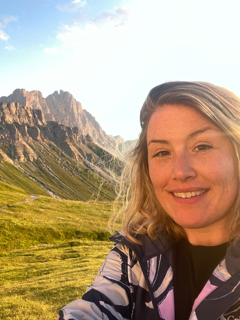 Hiker selfie at Schlüterhütte: Close-up of a smiling hiker during golden hour with dramatic Dolomite cliffs behind, taken near Rifugio Schlüterhütte on Day 2 of Alta Via 2.
