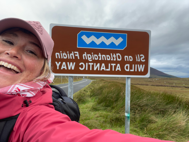 A hiker smiles with the Wild Atlantic way sign behind her