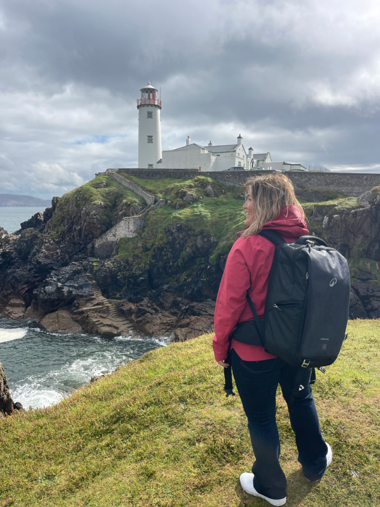Woman in red jacket looks out on to the seashore of fanad lighthouse