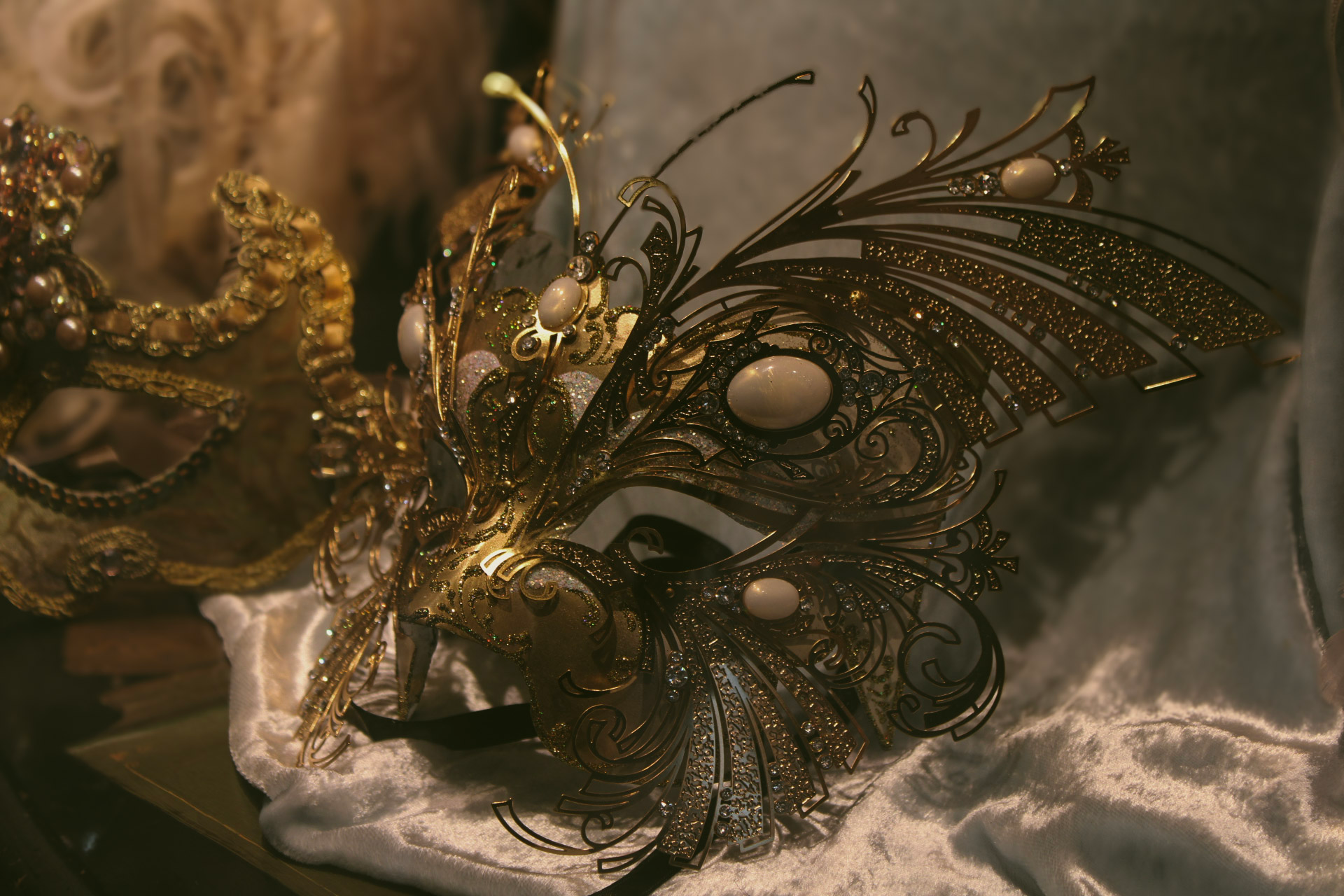 a golden carnivale mask with glitter and feathers sits on a silk cloth in dim lighting during Venice's Carnivale