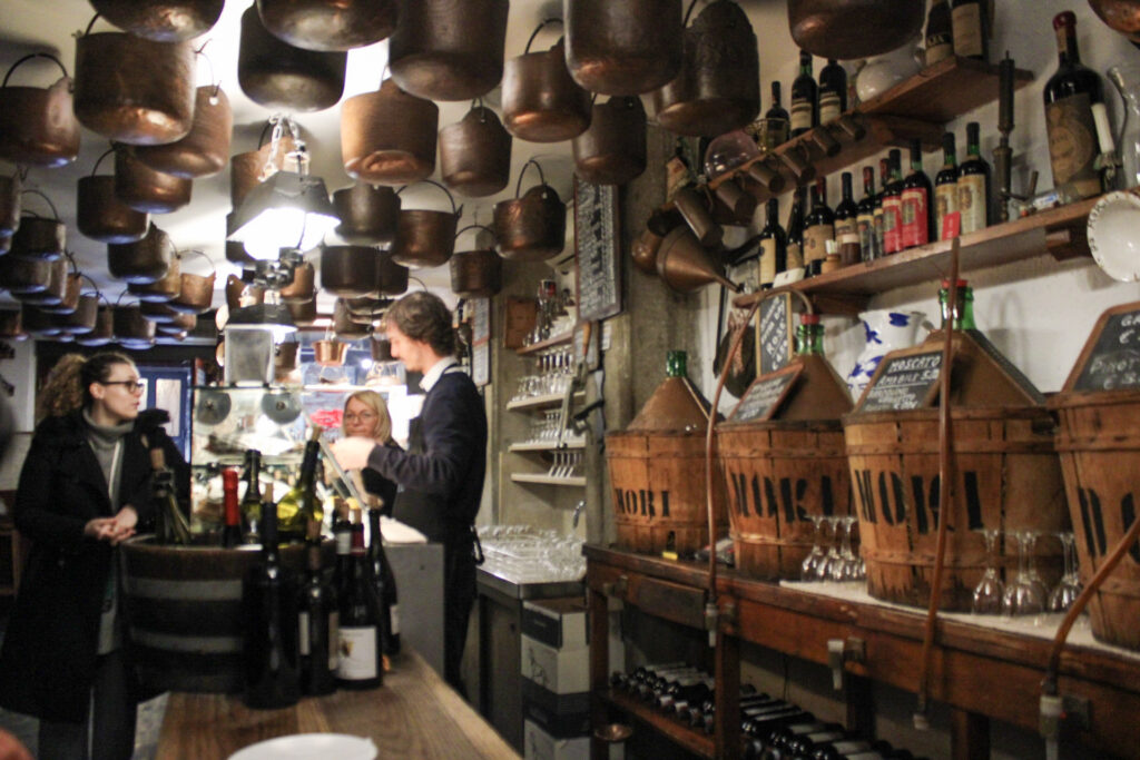 interior of Cantina Do Mori with various demi jons and chicchetti lining a refridgerated section while a worker helps a hungry person
