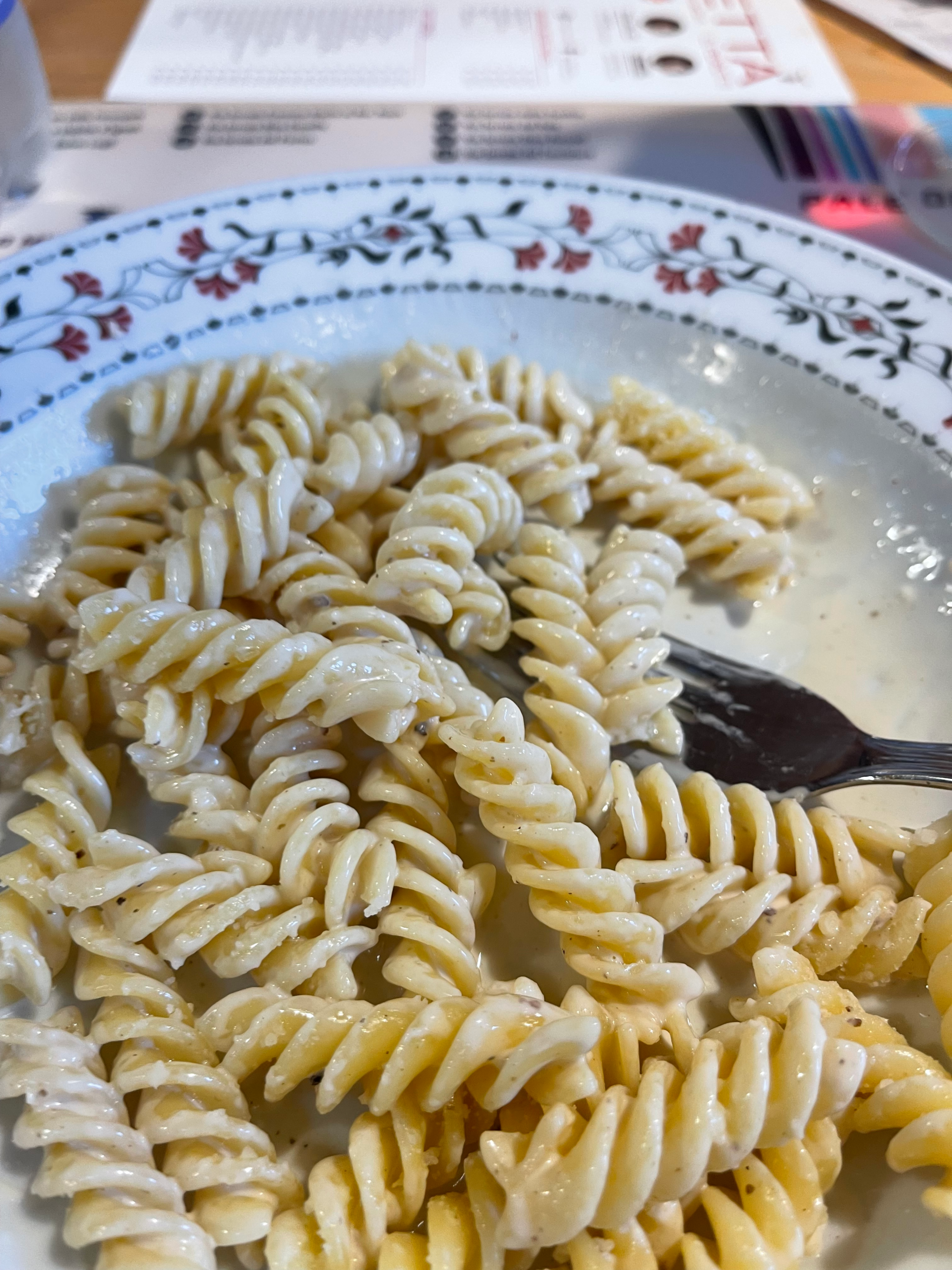 Close-up of creamy cacio e pepe fusilli pasta served at Rifugio Rosetta on the Palaronda Trek. The twisted noodles are coated in a rich cheese and black pepper sauce, plated on a floral-patterned dish.