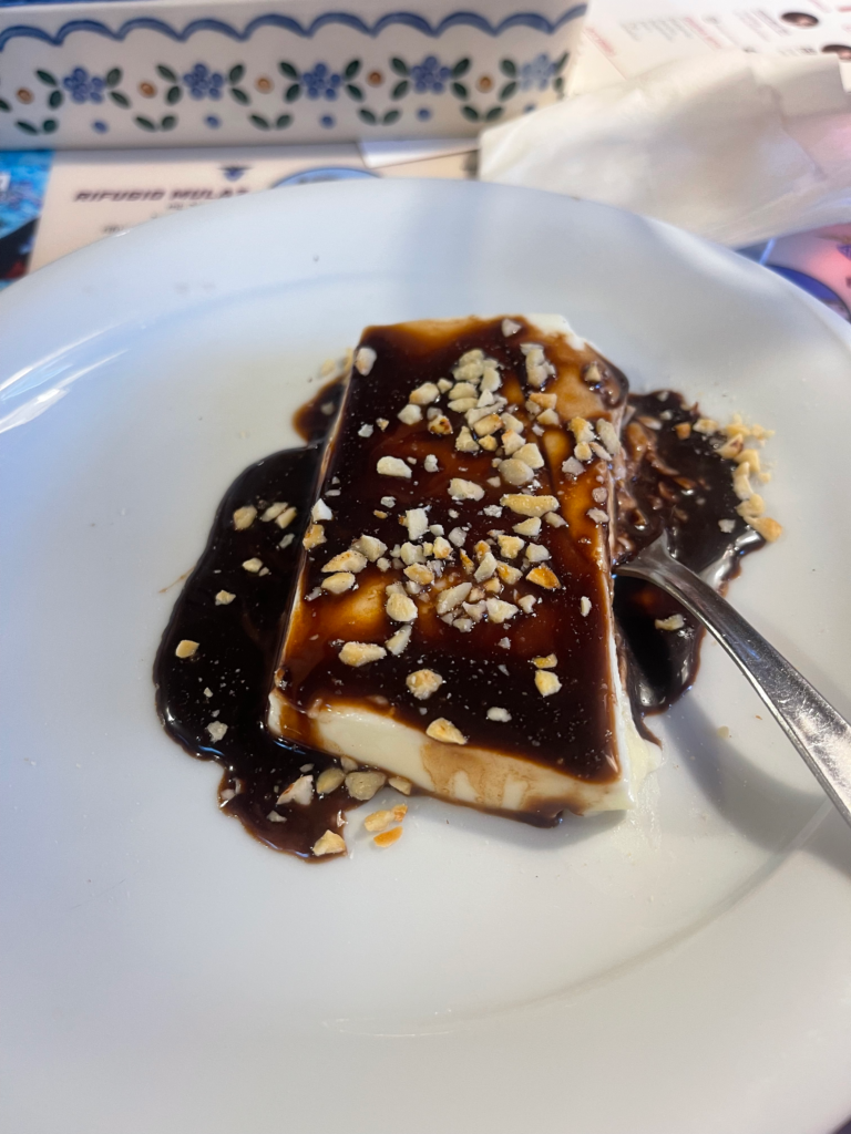 Panna Cotta served with chocolate sauce and hazelnuts on a white plate on day 3 dinner Rifugio Treviso