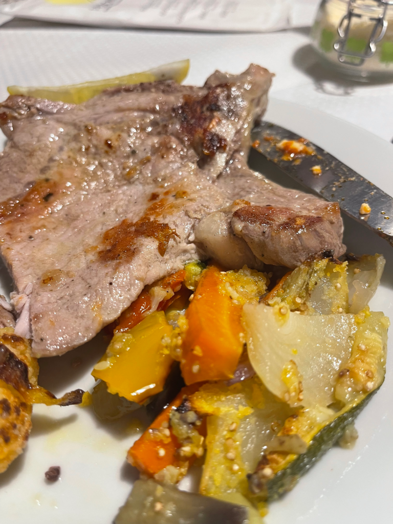 Grilled pork chop served at Rifugio Treviso, paired with a colorful medley of roasted vegetables including carrots, zucchini, onions, and bell peppers, all lightly seasoned and drizzled with olive oil.