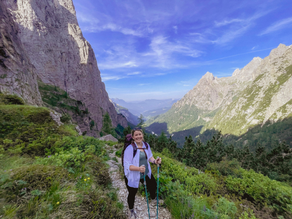 woman in white hiking shirt, trekking poles in hand and smiling at the camera while hiking Val Canali on the Palaronda Trek in the Dolomites