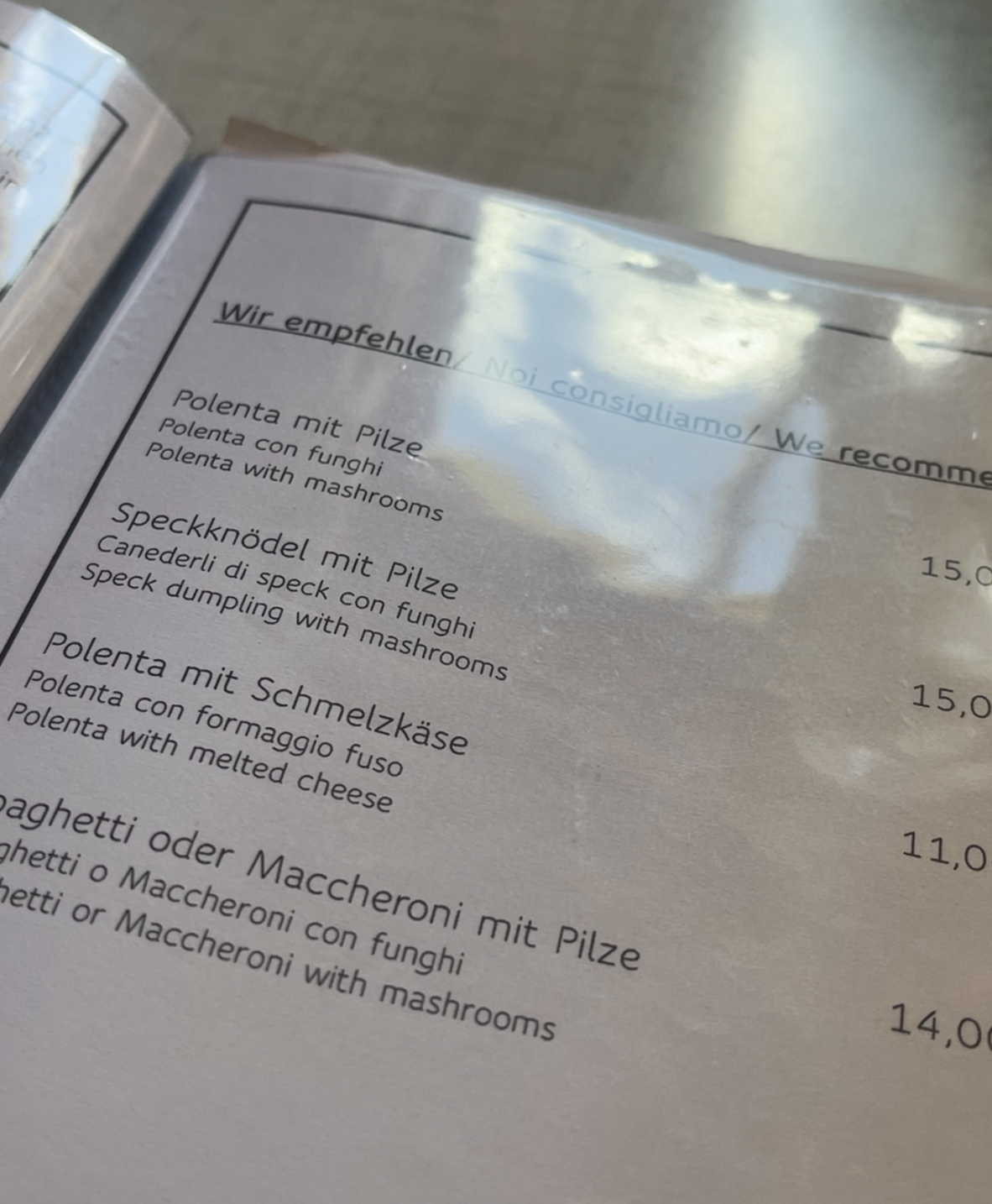 Menu from summer 2024 at Rifugio Genova/Schlüterhütte, showing recommended dishes in German, Italian, and English. Visible items include polenta with mushrooms, speck dumpling with mushrooms, polenta with melted cheese, and spaghetti or maccheroni with mushrooms, with prices listed in euros.