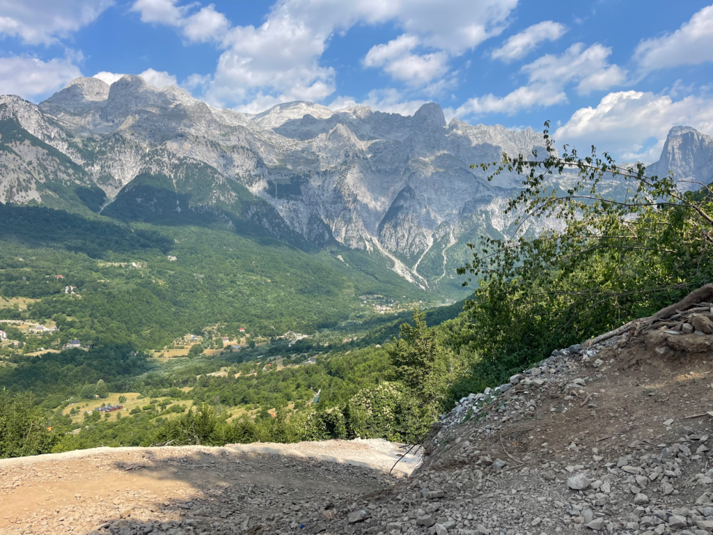 a dirt trail stretches beyond the camera and a wide shot of mountains is beyond the trail in Theth Albania