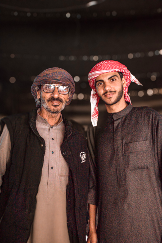 two men from wadi rum smile at the camera in traditional bedouin gear.