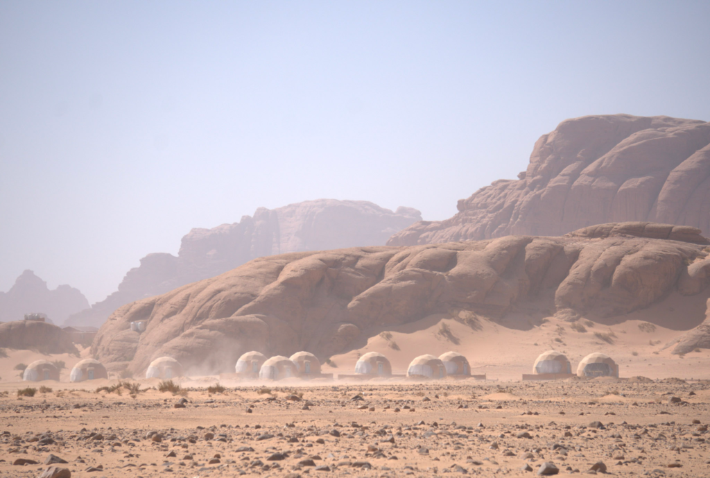 the desert of wadi rum during mid day with glamping hotel bubbles in the distance
