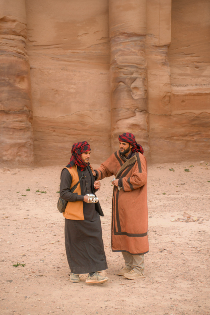 two men console one another with jewlery in their hands, they are wearing long coats with head wraps