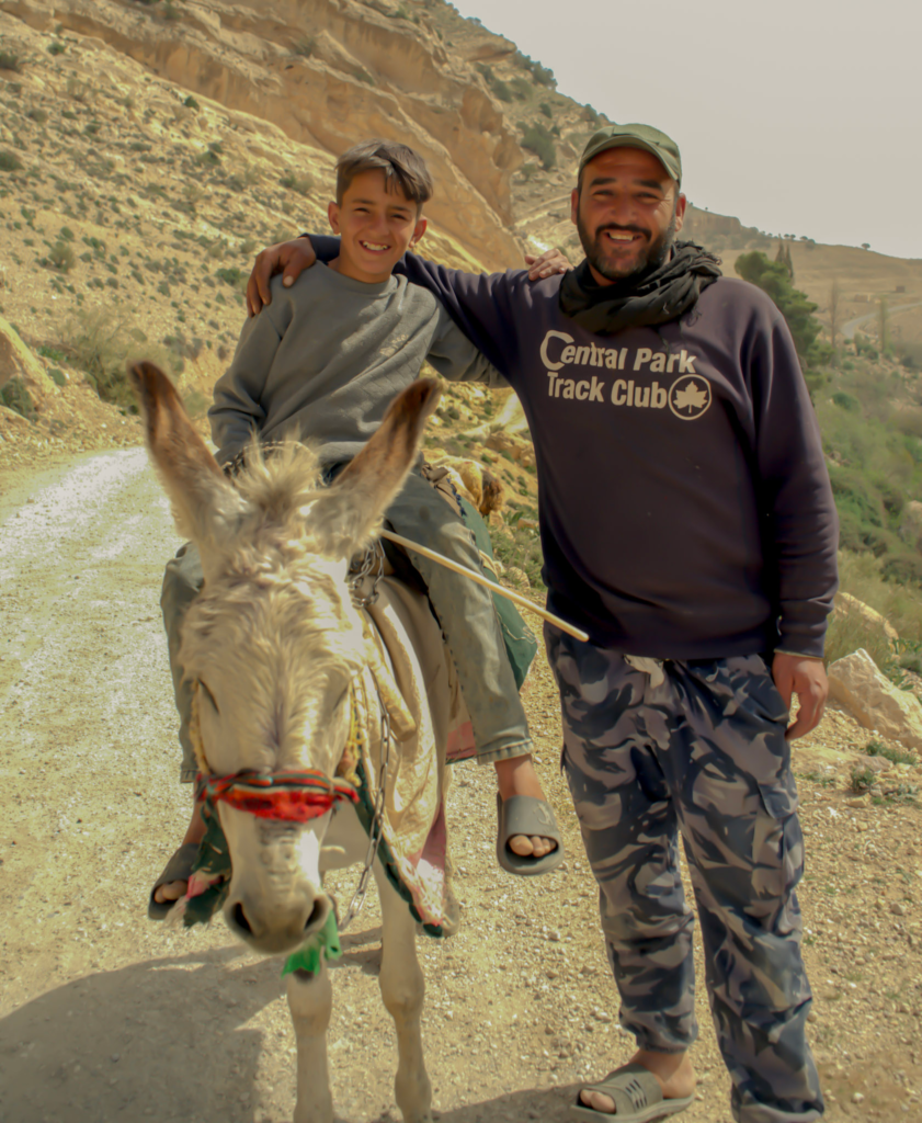 a young boy sits on a donkey with an older man in the Dana Biosphere.