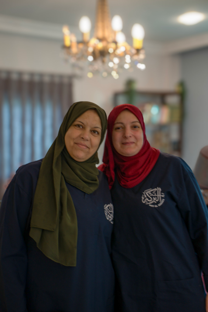 two women in hijabs and a uniform of beit al baraka smile for the camera