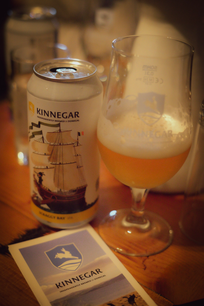 a glass with a bit of beer in it and a phamplet that says Kinnegar next to a can