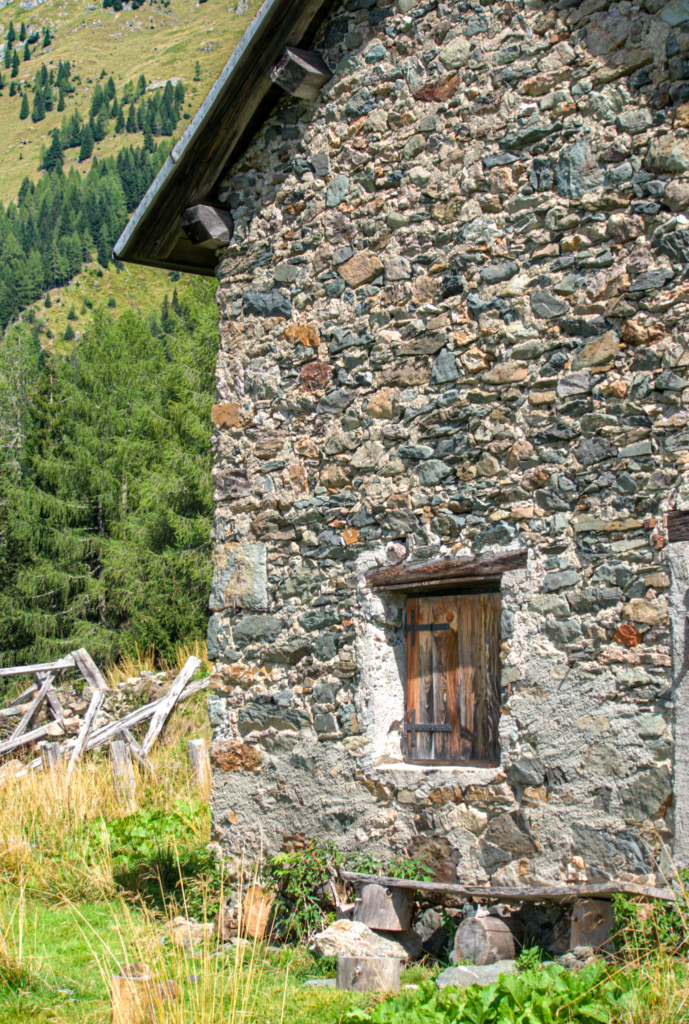 a stone house with boarded doors and green grass surrounding it