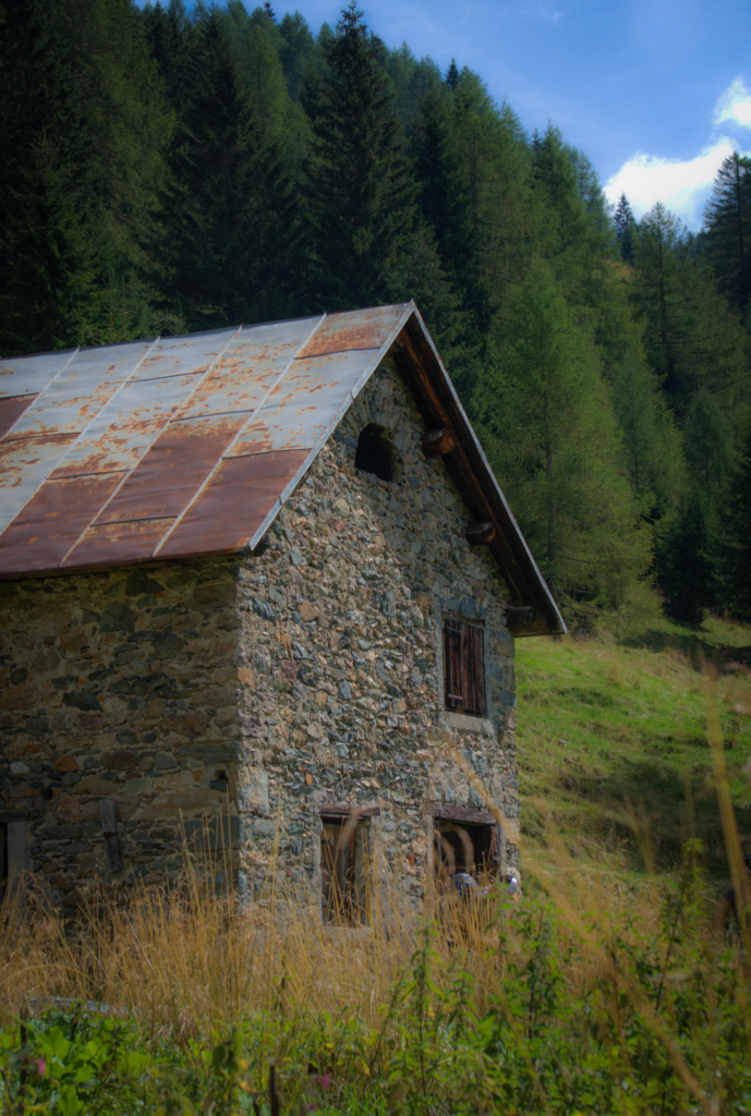 a stone house in the Carnic alps with a rusted roof surrounded by green grass