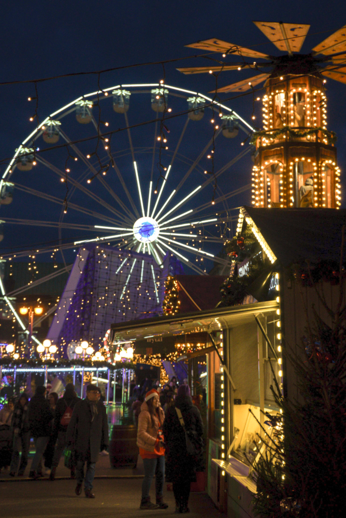 a giant ferris wheel sits in the background lit up next to the poznan christmas market stalls