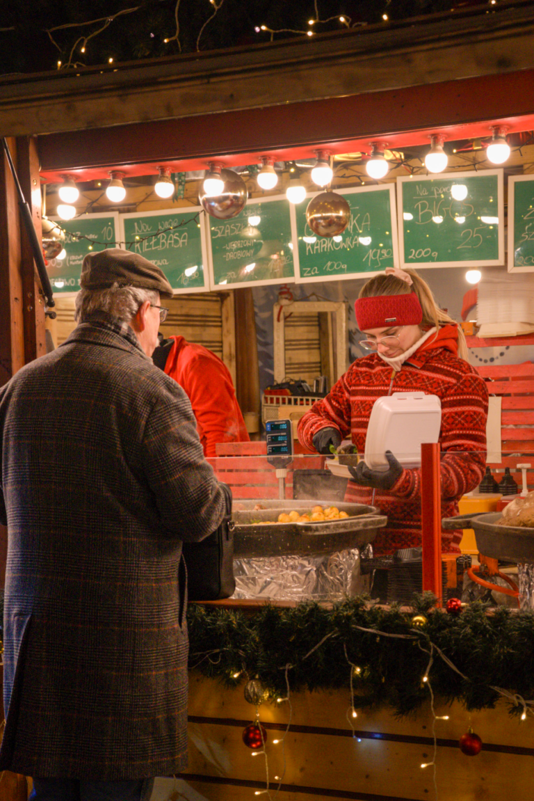 a man ordering meat from a festive christmas market stall as a woman packs up food for him in a bag at the Poznan Christmas Market