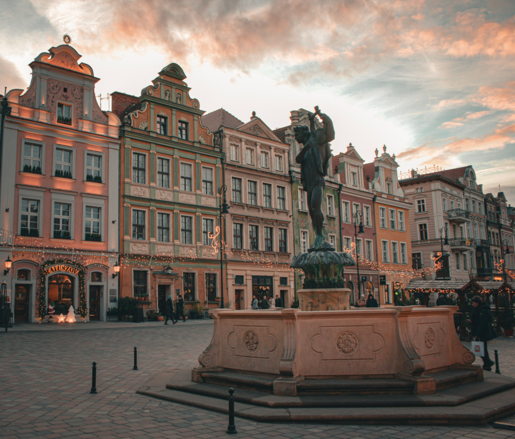 Colorful historic buildings and the Neptune Fountain overlook a cobblestone plaza draped in Christmas lights. This scene captures the charm of Old Market Square during the Poznan Christmas Market in Poland.