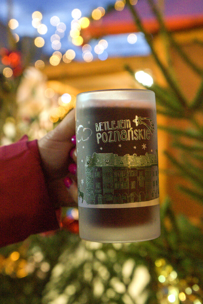 A big glass of mulled wine with a hand holding it, christmas tree behind it blured out.