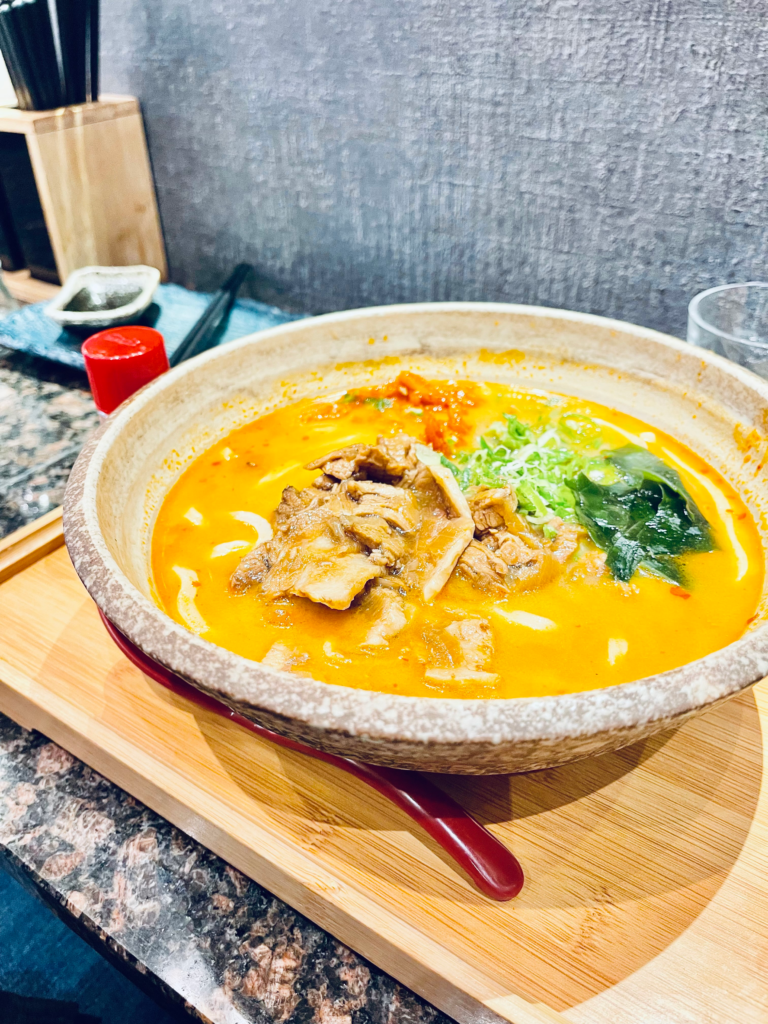 a bowl of ramen with orange broth and various vegetables on top