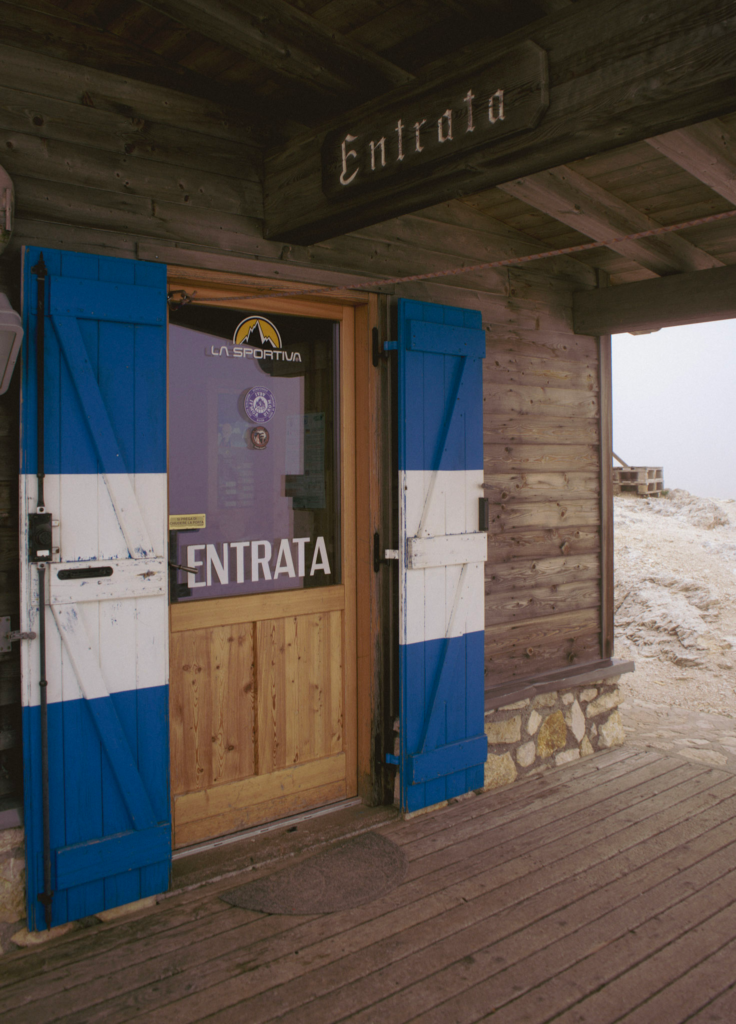 Front door of Rifugio Rosetta with blue and white shutter doors on a foggy day