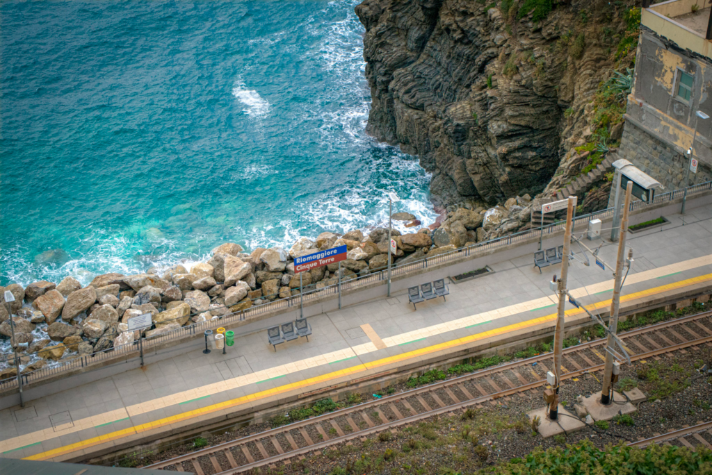 an arial view of the Riomaggiore train station in Cinque Terre with the blue ocean crashing against the rocks