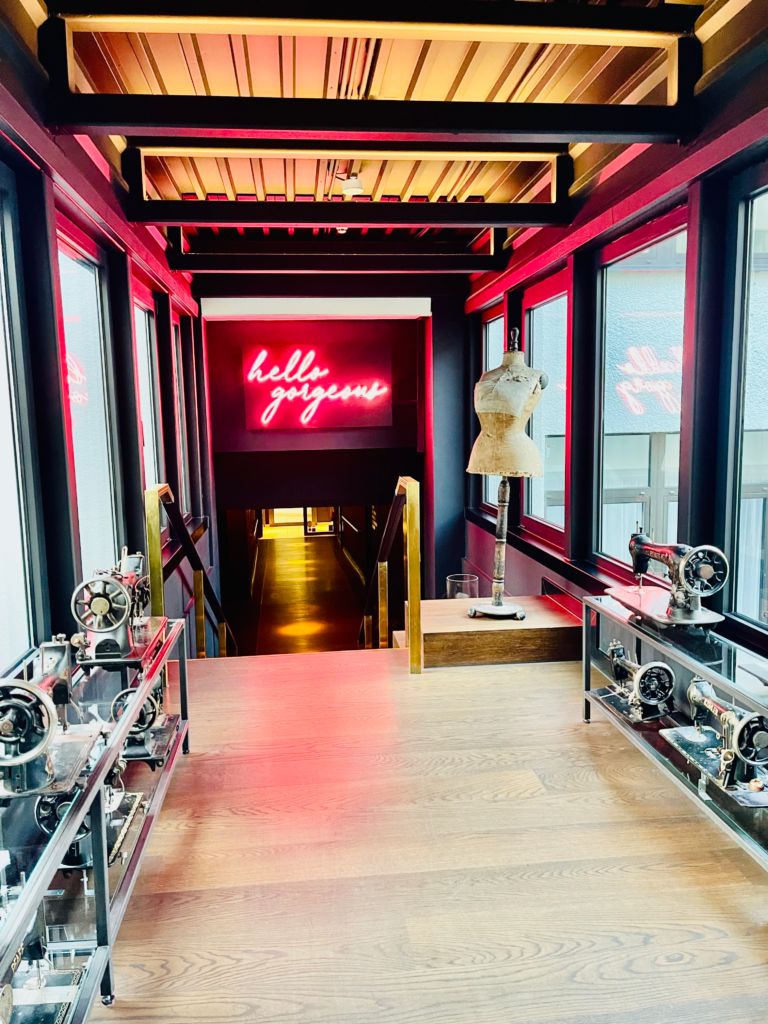 Brightly lit Corridor of Ruby Coco Hotel with sewing machines lining the hallway and a bright sign saying "bye Gorgeous"