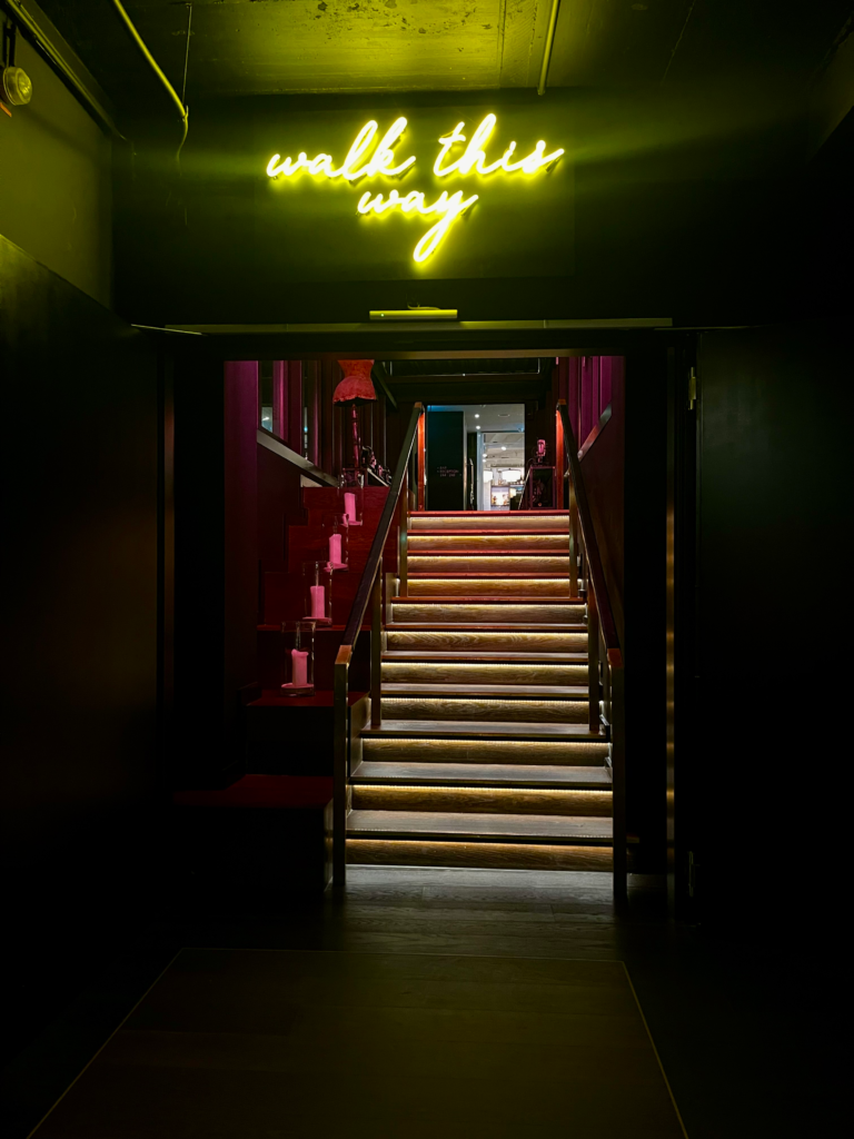 dark interior of a hotel lobby in dussedorf that has a neon sigh "WALK THIS WAY"