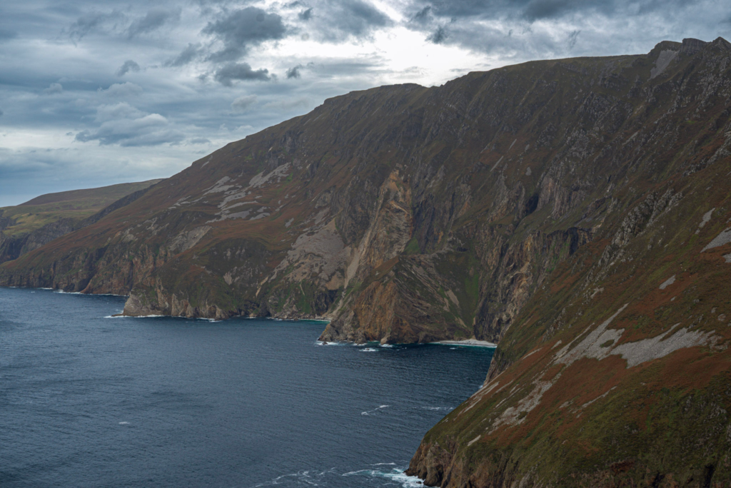 vast cliffs stretch out before the photo with sprinkles of orange and green with the ocean below at the Slieve Leagues