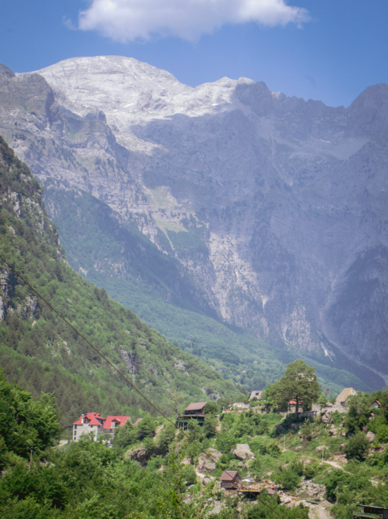 a small village in the distance near theth valbone valley with an imposing mountain range or the Acursed mountains of Albania