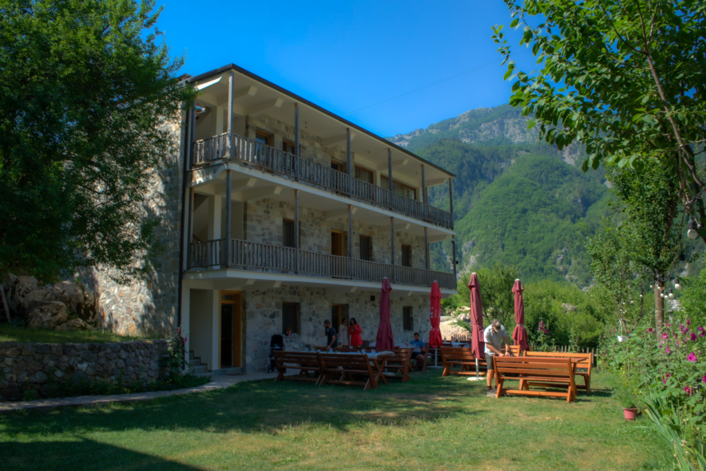 a three story guesthouse with picnic tables outside in Theth, Albania