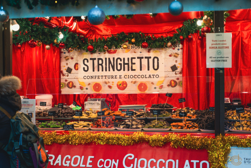 a sign that says stringhetto with a display of chocolates next to it . A Sign on a poll says OUR PRODUCTS ARE GLUTEN FREE