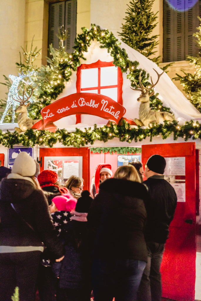 a festive christmas market scene with people lined up to visit Babo Natale at the Verona Christmas Market