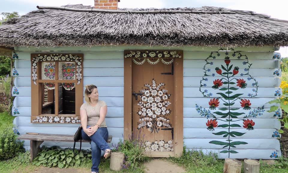Woman looking away from camera smiling while sitting front of a florally decorated traditional house in Zalipie Poland