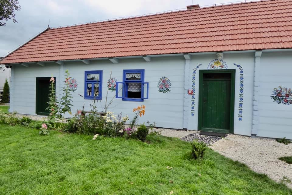 a traditional house in Zalipie Poland that has a white exterior and red roof. The house has blue, green and pink flowers painted on it in Zalipie Poland