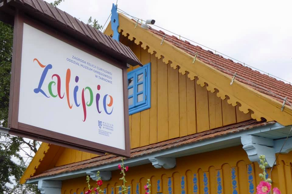 a colorful sign that says Zalipie with a brown and blue house ebhind it