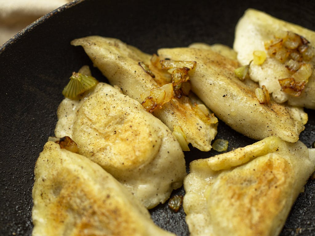 Appetizing fried dumplings with onions in a frying pan, showcasing traditional cuisine.