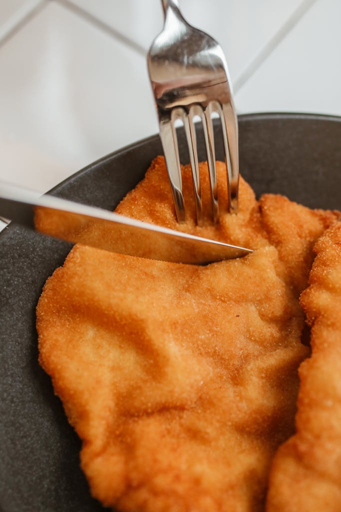 Close-up of a crispy fried cutlet on a plate with fork and knife.