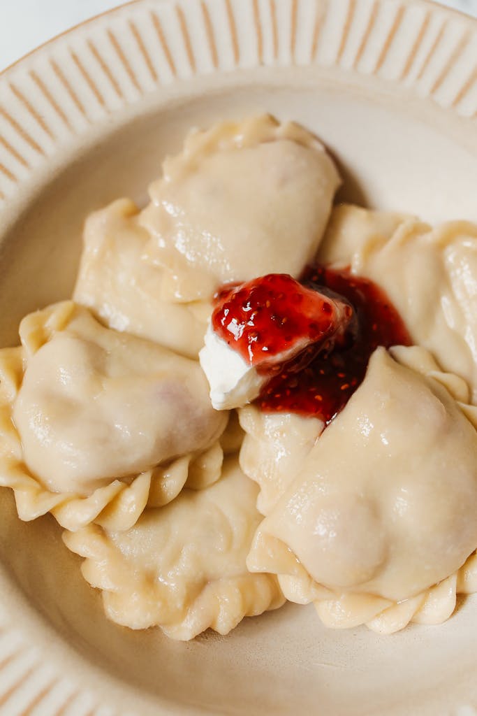 Delicious pierogi with strawberry jam and cream on a plate, close-up shot.