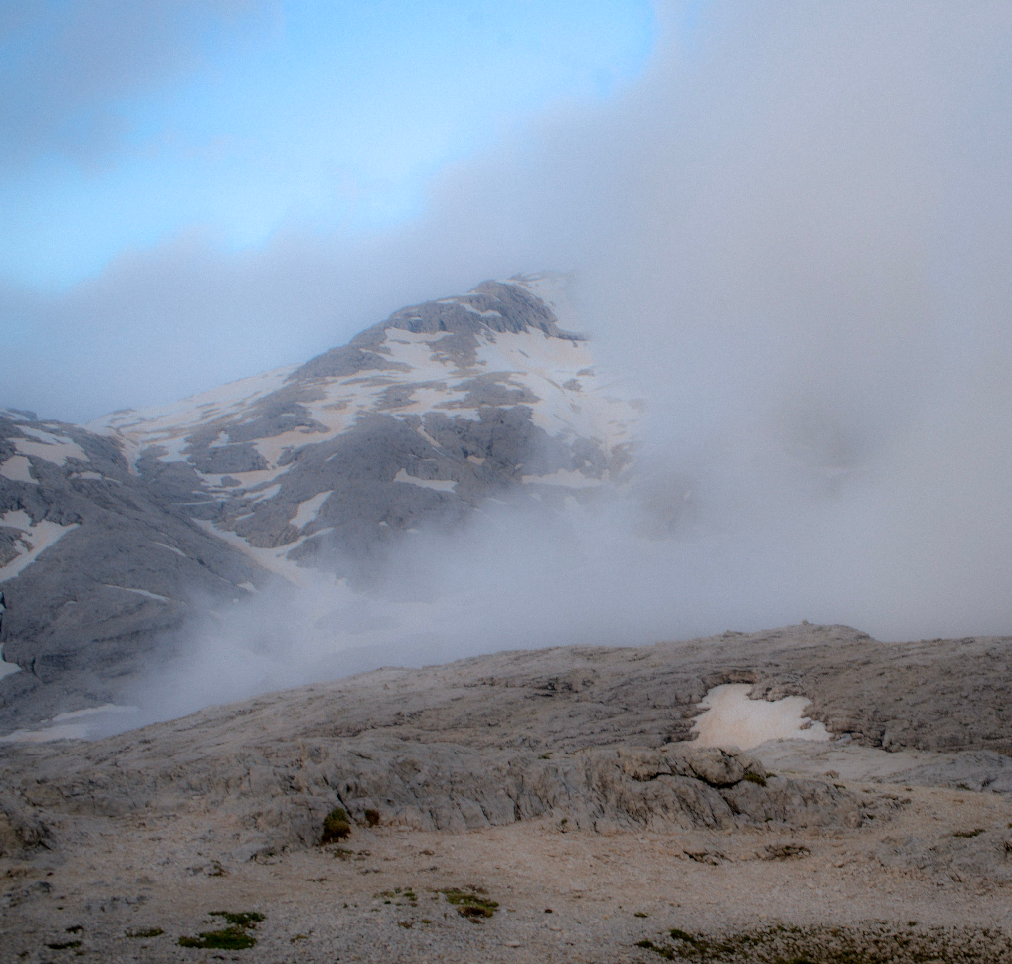 mountain covered in fog with little blue sky coming through and lunar landscape of Fradusta Glacier