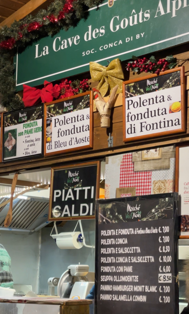 a christmas market stall with various signs with writing in italian, swiss and french with different food items and their prices