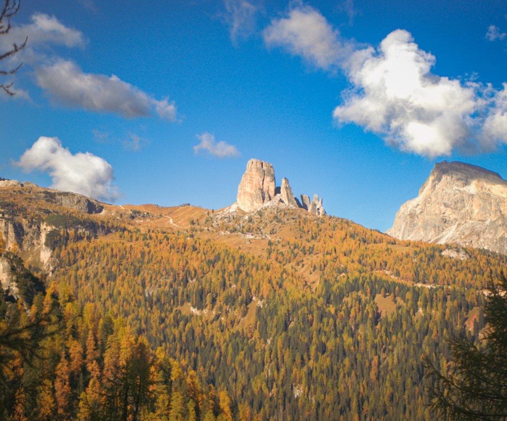 Cinque Torri juts up from the mountainside on a fall day in the dolomites surrounded by larches turning orange